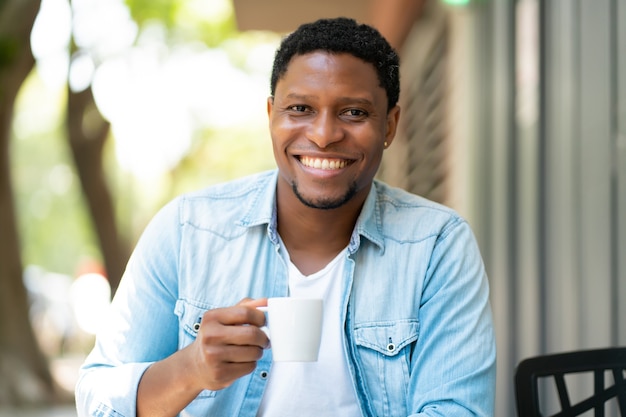 아프리카 계 미국인 남자 즐기는 야외 커피 숍에 앉아있는 동안 커피를 마시는. 도시 개념.