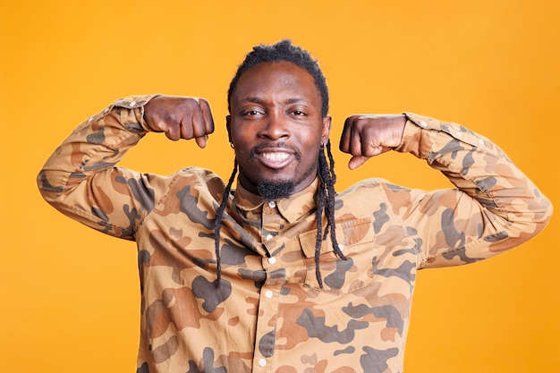 African american man flexing triceps strength before workout training in studio over yellow background. Confident athletic person posing to show biceps, muscular body from fitness