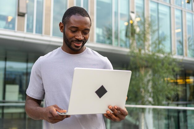 African american man freelancer using laptop typing chatting on urban street in city guy having