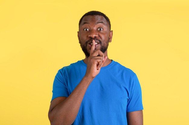 African american man gesturing hush sign posing over yellow background