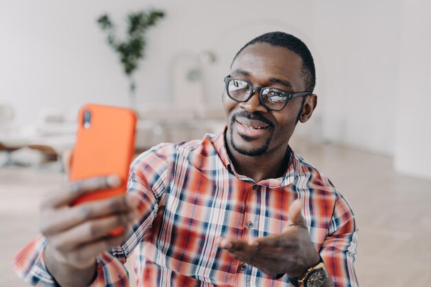 Афроамериканец в очках, держащий смартфон, использует современные приложения, разговаривает онлайн по видеозвонку