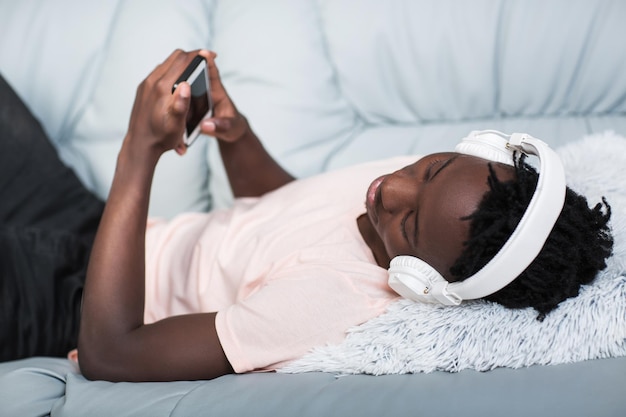 African-American man in headphones lying on the couch and listening to music