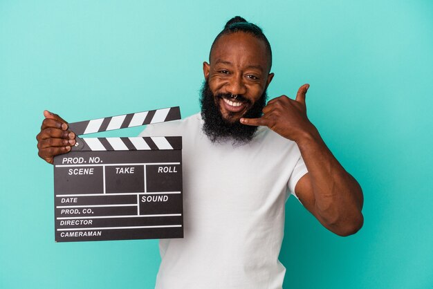 African american man holding clapperboard isolated on blue background showing a mobile phone call gesture with fingers.