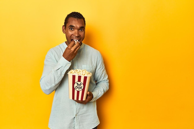 African American man holding popcorn in yellow studio backdrop