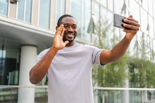アフリカ系アメリカ人の男性がスマートフォンを持って街の街でビデオチャットをしている男のブロガー