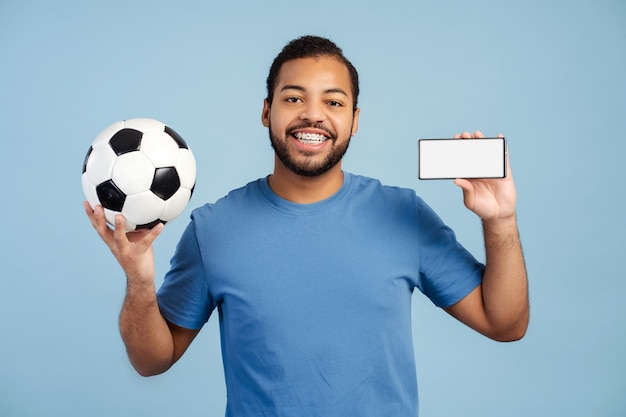 African American man holding soccer ball and mobile phone with empty screen looking at the camera