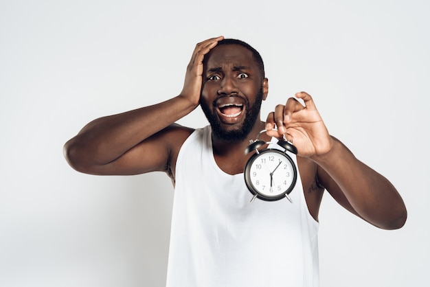 African American man holds head with alarm clock