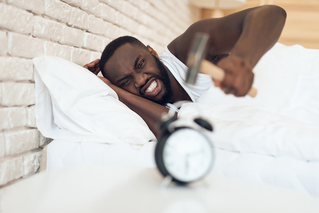 African American man is hammering alarm clock. Waking up.