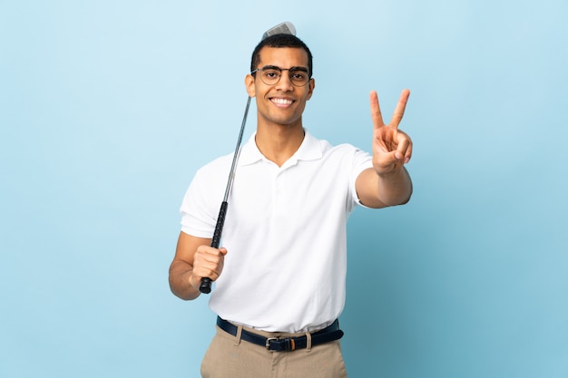 African American man over isolated blue wall playing golf and and showing victory sign