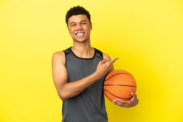 バスケットボールをし、側面を指している黄色の背景に分離されたアフリカ系アメリカ人の男