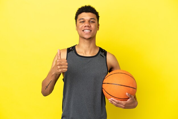 Афро-американский мужчина, изолированные на желтом фоне, играет в баскетбол и с большим пальцем вверх