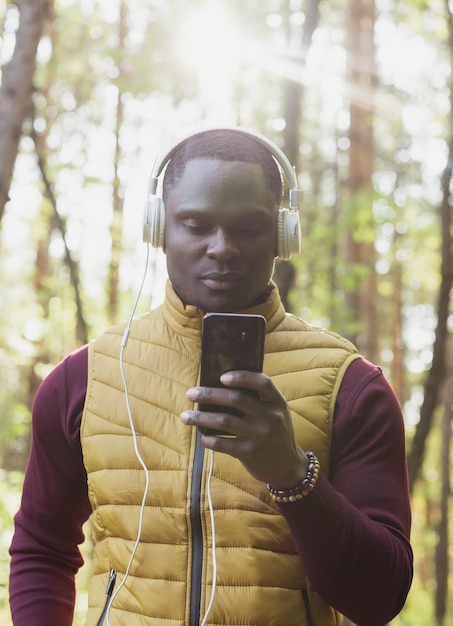 アフリカ系アメリカ人男性が秋の公園で音楽を聴くガジェットアプリとストリーミングサービスのコンセプト