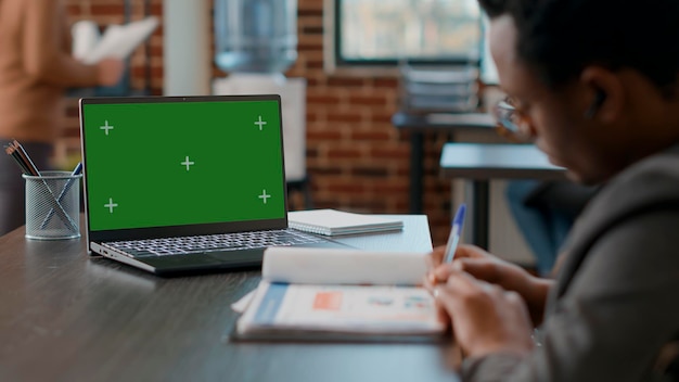 African american man looking at laptop with greenscreen in disability friendly office. consultant taking notes and using chromakey copyspace with isolated mockup template and blank background