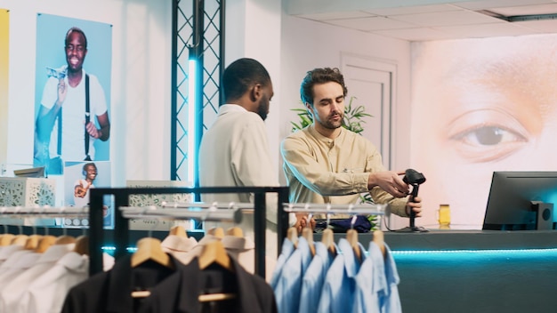 African american man paying for new modern clothes, making transaction on pos terminal in shopping center. Male client talking to store assistant at cash register, commercial activity. Handheld shot.