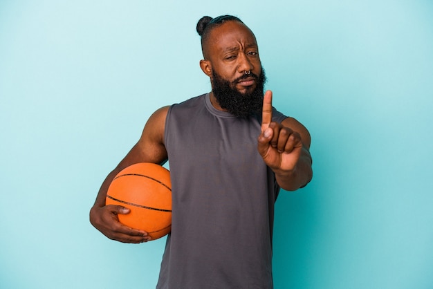 Афро-американский мужчина играет в баскетбол на синем фоне, показывая номер один пальцем.