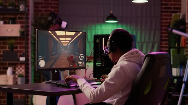 African american man playing online first person shooter while gaming girl is fighting in virtual reality game. Gamer streaming multiplayer action game on pc while girlfriend uses vr goggles.