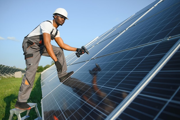 African american man in safety helmet and glasses tighten nuts on solar panels with screwdriver Competent technician using tools while performing service work on station