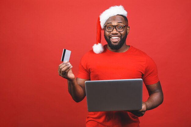 African American man in Santa Claus hat holding laptop