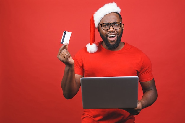 African American man in Santa Claus hat holding laptop
