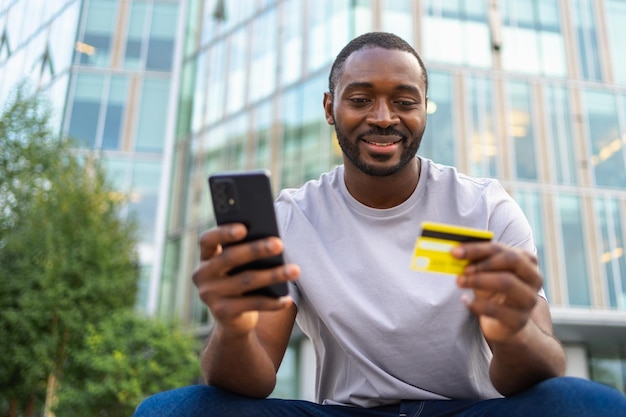 Foto uomo afroamericano che compra online con uno smartphone che paga con una carta di credito d'oro.