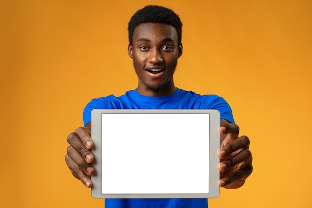 노란색 스튜디오에 복사 공간이 있는 빈 디지털 태블릿 화면을 보여주는 아프리카계 미국인 남자