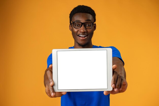 African american man showing blank digital tablet screen with copy space in yellow studio