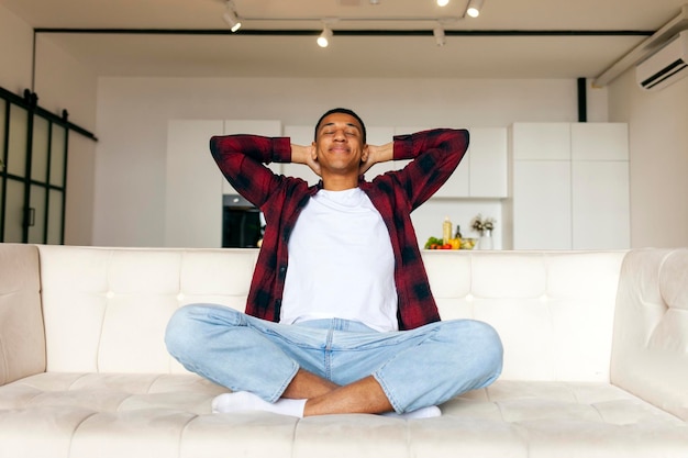 Photo african american man sits on comfortable sofa at home and rests guy relaxes and smiles on the couch