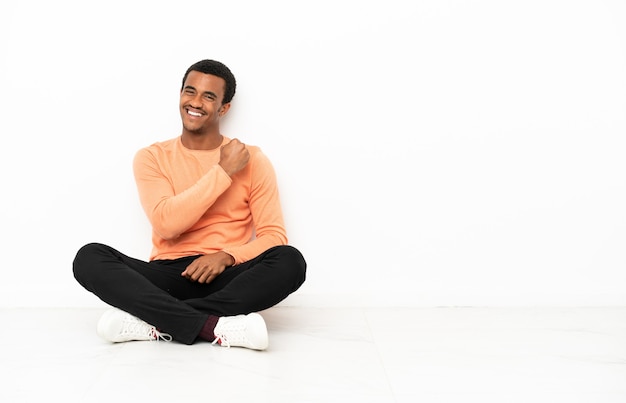 African American man sitting on the floor over isolated copyspace background celebrating a victory