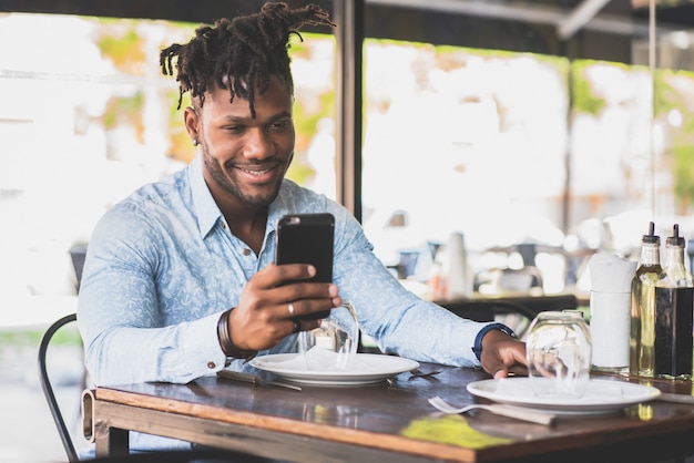 African American man smiling while using a mobile phone at a restaurant.