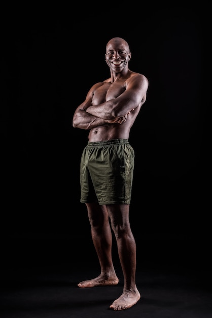 African American man standing in shorts with arms crossed in a black background