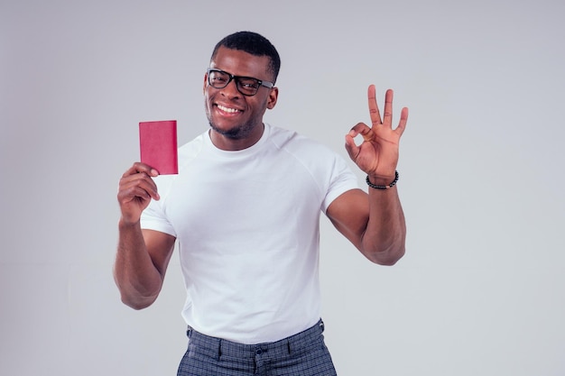 African american man student in a white T-shirt and glasses holding passport red cover