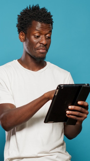 Uomo afroamericano che utilizza tablet digitale e sorride durante la digitazione sul touchscreen. persona di colore con un dispositivo moderno per messaggi di testo e comunicazione utilizzando la tecnologia e ridendo