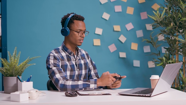 African american man using joystick on laptop to play video\
games, feeling happy about online competition. modern person\
playing game with controller and headphones on computer\
console.