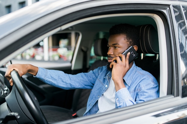 Uomo afroamericano che utilizza smartphone che fa chiamata cellulare mobile durante il tempo di guida in auto di lusso preferite.