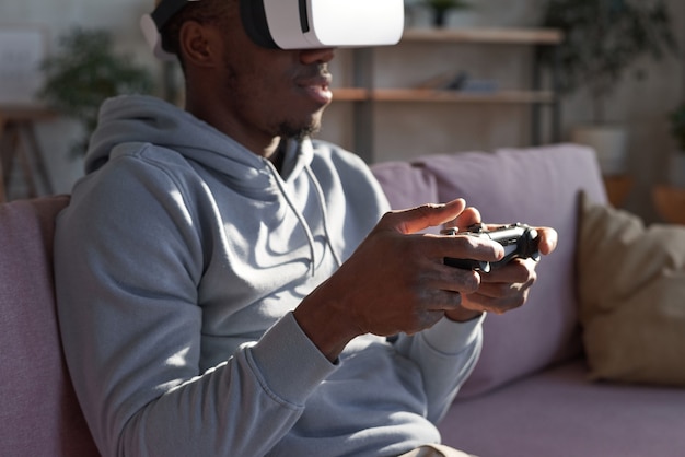 Афро-американский мужчина в гарнитуре виртуальной реальности играет в интерактивную компьютерную игру в помещении