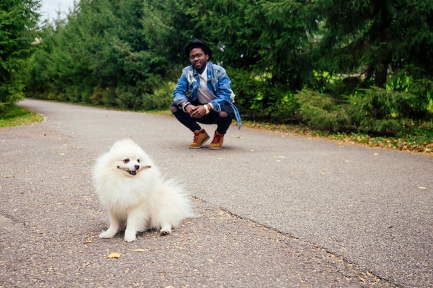 ふわふわのスピッツを持って通りを歩いているアフリカ系アメリカ人の男が、教育犬のチームを教えています。