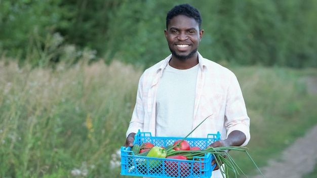 アフリカ系アメリカ人男性が木のそばの箱に農場の収穫物を持って歩く