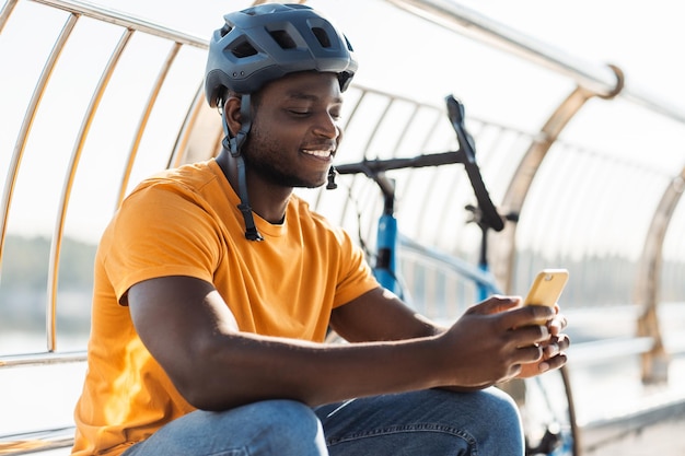 안전 헬을 착용 한 아프리카계 미국인 남자가 휴대전화를 들고 야외에서 온라인 쇼핑을 하고 있습니다.