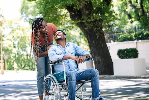 An african american man in a wheelchair enjoying a walk outdoors with his girlfriend.