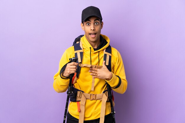 African American man with backpack and trekking poles over isolated wall pointing to oneself