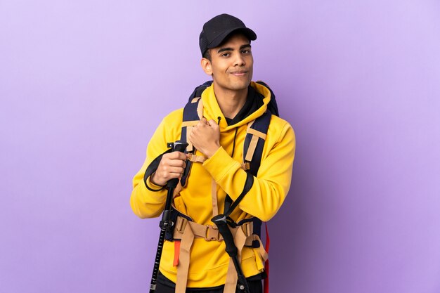 African American man with backpack and trekking poles over isolated wall proud and self-satisfied