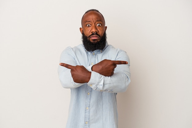 African american man with beard isolated on pink wall points sideways, is trying to choose between two options.