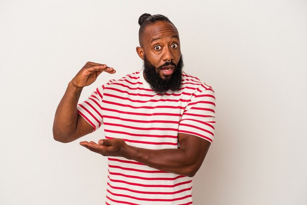 African american man with beard isolated on pink wall shocked and amazed holding a copy space between hands.