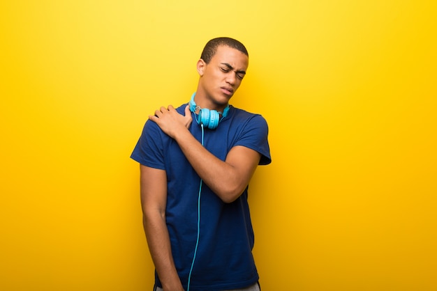 Uomo afroamericano con la maglietta blu su fondo giallo che soffre dal dolore