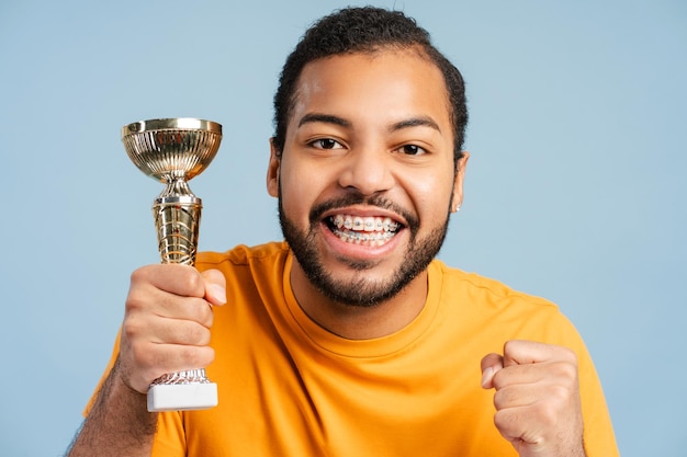 African American man with dental braces holding trophy his fist clenched in a victory gesture