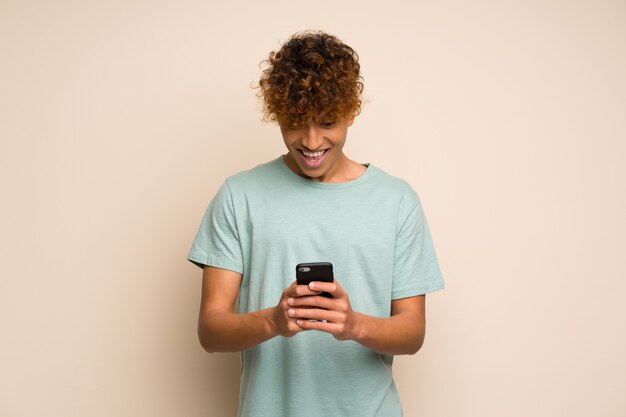 Uomo afroamericano con la camicia verde sorpreso e inviando un messaggio