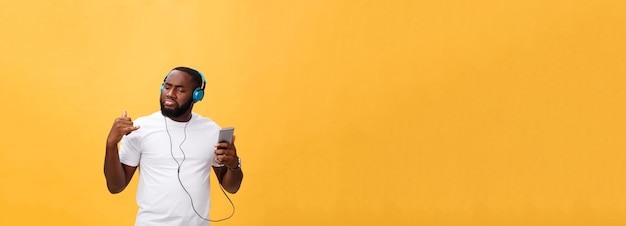 African american man with headphones listen and dance with music isolated on yellow background