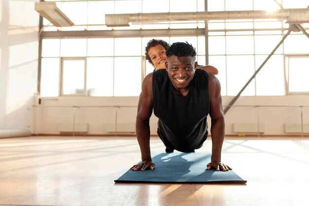 african american man with his son goes in for sports in the gym dad does pushups from the floor