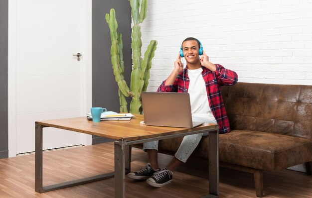 Uomo afroamericano con il computer portatile nel salone che ascolta la musica con le cuffie