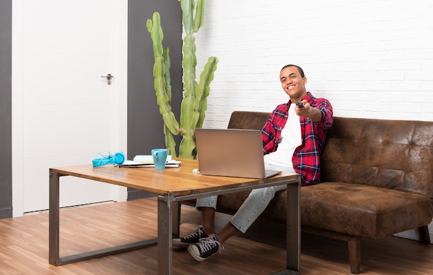 African american man with laptop in the living room with a television remote